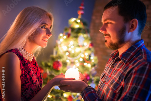 Beautiful young couple man and woman holding a glowing ball in their hands against the background of Christmas decorations. The concept of a happy family life and joint holidays