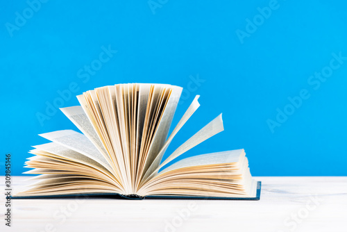 Composition with vintage old hardback books, diary, fanned pages on wooden deck table and blue background. Stacking books. Back to school. Copy space education