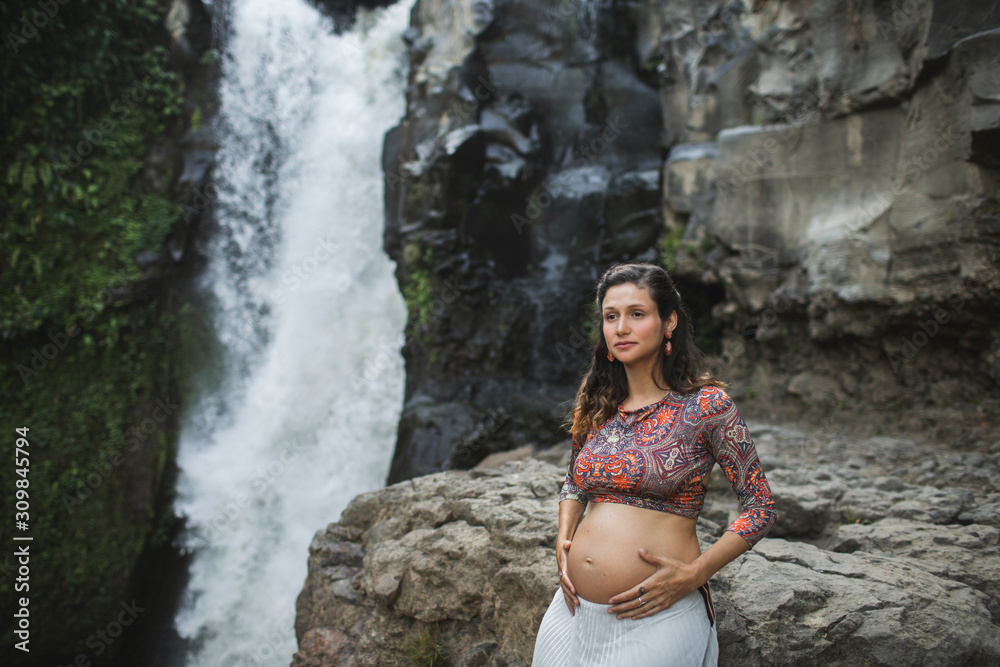 Young happy latin pregnant woman enjoying maternity and nature outdoor. Holding naked belly. Harmony with nature, childbirth in Bali travel. Spiritual maternity happiness.