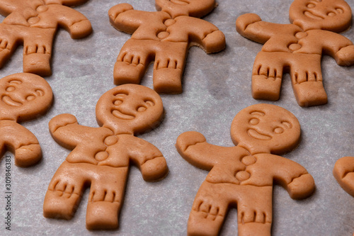 set of raw dough with smiling gingerbread men on baking paper background ready for the oven, traditional homemade biscuit for Christmas time and new year