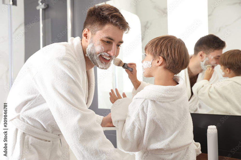 Obraz premium Dad and son with shaving foam on their faces having fun in bathroom
