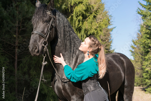 Woman holds her black horse in forest, outdoors photo.