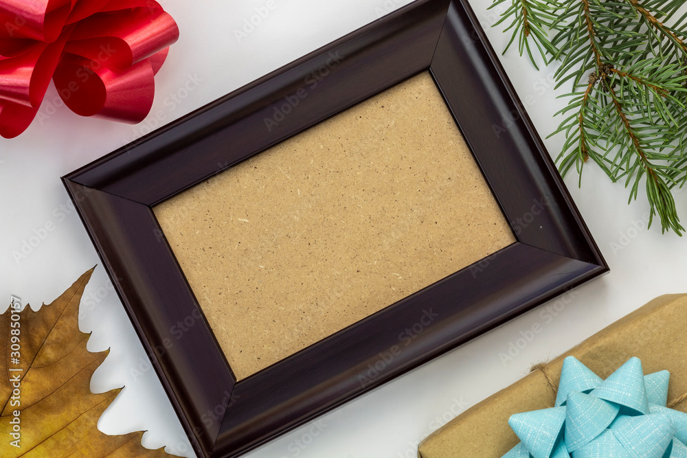 Fototapeta premium Composition Using Empty Picture Frame, Decorative Bow, Pine Branch, Gift Box, and Dry Autumn Leaf on White Background