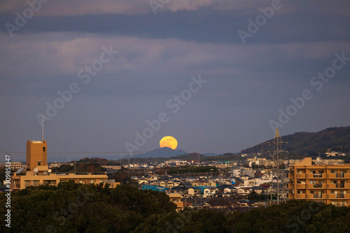 Full moon rises over distant mountain in small Japanese town at dusk
