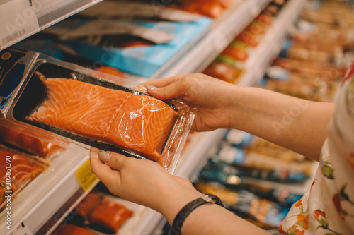 A young girl chooses food while shopping in the mall in the fish department. Fresh red trout on the top shelf of the counter.