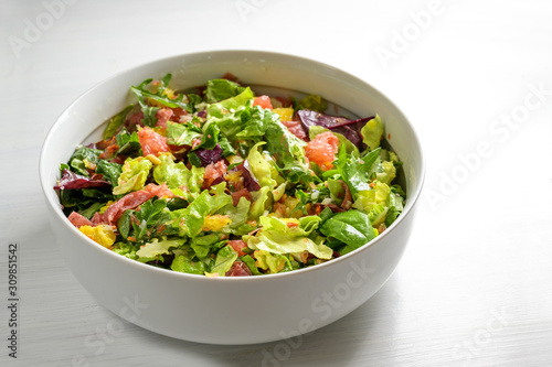 Healthy mixed salad of lettuce, orange, grapefruit, salami and pine nuts in a large bowl, gray to white background with copy space