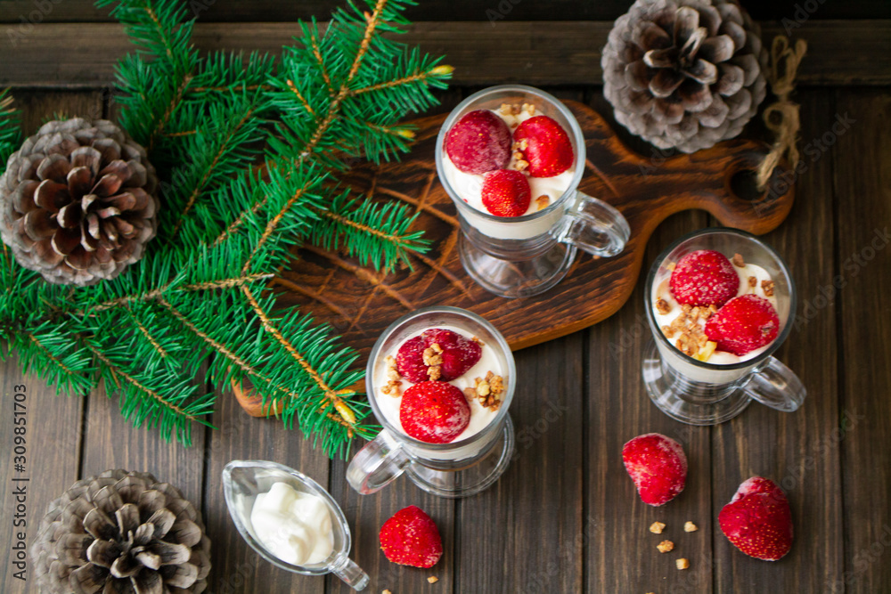 Healthy strawberry parfaits in glass pubs on rustic wooden table decorated by spruce branch and pine cones for holiday Healthy strawberry parfaits in glass pubs on rustic wooden table decorated by spruce branch and pine cones for holiday
