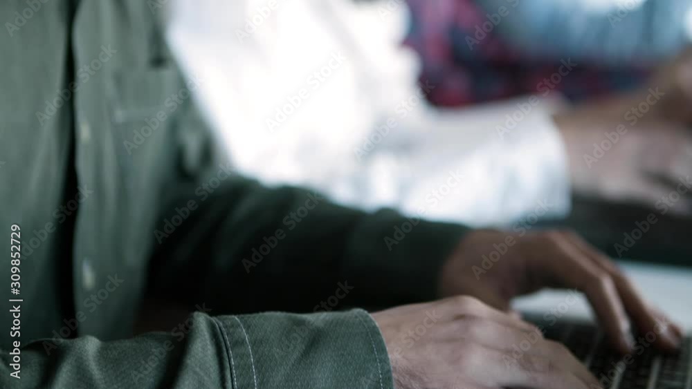 Side view of focused developer in eyeglasses working with laptop. Young people sitting in row and typing on laptops. Technology concept Side view of focused developer in eyeglasses working with laptop. Young people sitting in row and typing on laptops. Technology concept