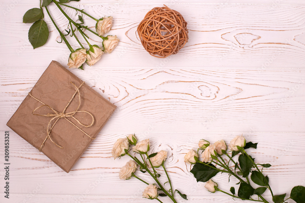 Gift box wrapped in kraft paper, rattan balls and flower on a white wooden background from above. Flat lay. Gift box wrapped in kraft paper, rattan balls and flower on a white wooden background from above. Flat lay.