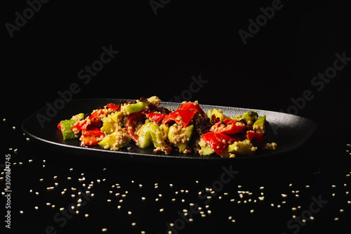 Raw paleo quinoa kale salad in a black plate on the dark background, with copy-paste space. Healthy, vegan, vegetarian and diet eating food.