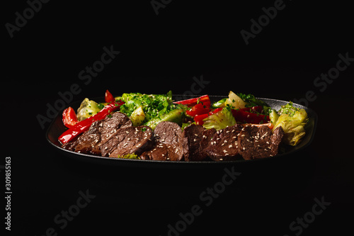 Juicy Beef Sirloin Steak Salad with bell pepper, sesam seeds and green vegetables in a black plate, on black background. Healthy food