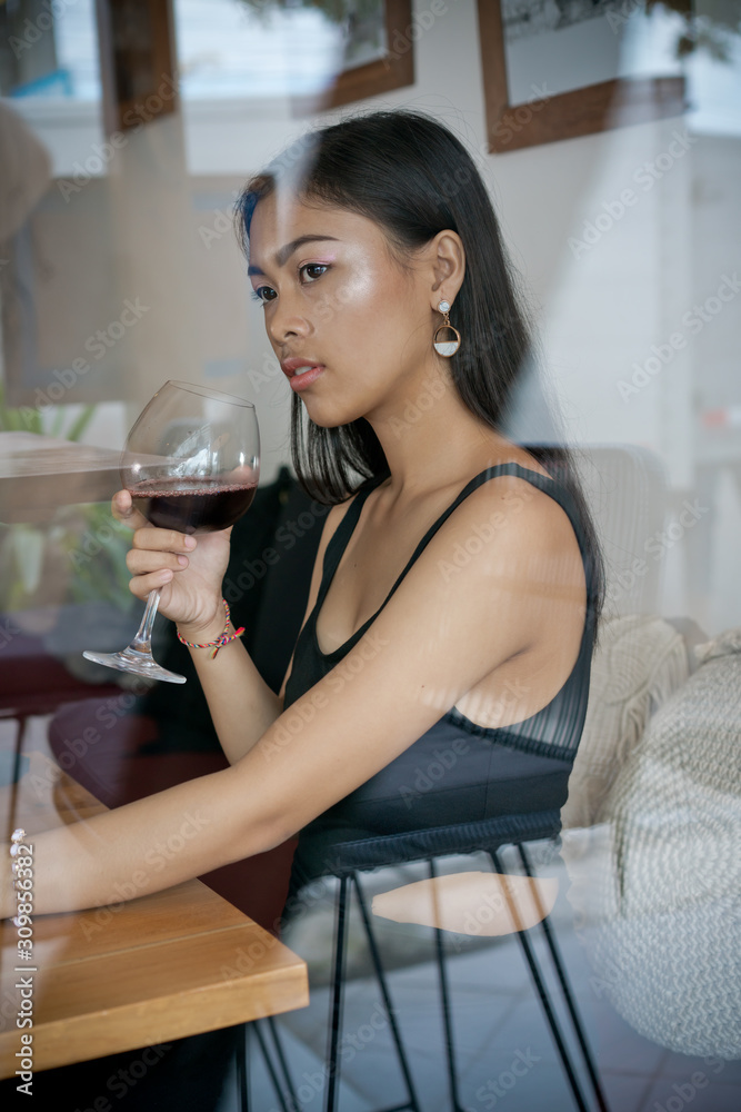 Asian girl in a cafe. Beautiful Balinese women with glass of wine with window reflection Asian girl in a cafe. Beautiful Balinese women with glass of wine with window reflection