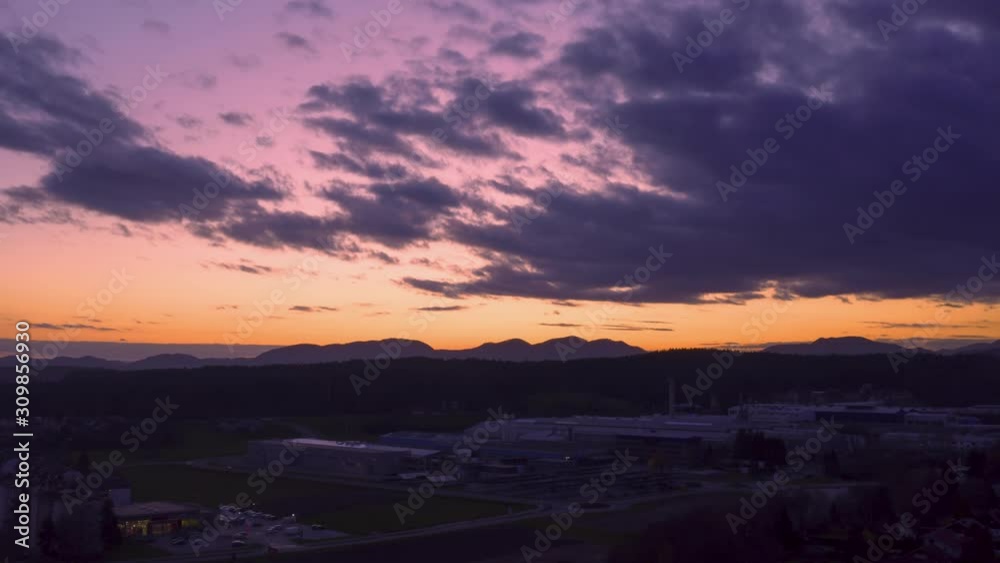 Dramatic rolling clouds in sunset time, hyper lapse of sundown above small town with a large factory Dramatic rolling clouds in sunset time, hyper lapse of sundown above small town with a large factory