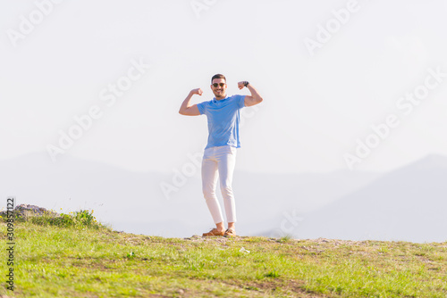 Well dressed ( fashionable) man stands in nature looking over a cliff at the large lake and mountain line while wearing boat shoes, polo shirt and formal pants.