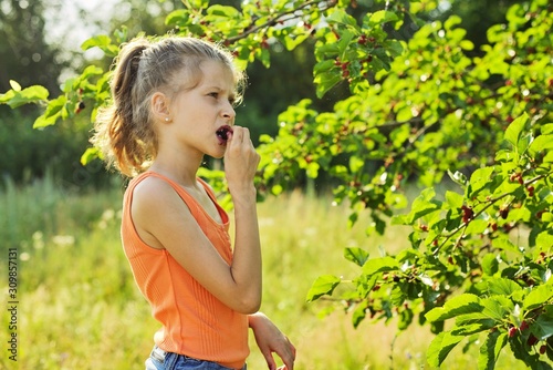 Girl with pleasure eating delicious sweet ripe berries from mulberry tree
