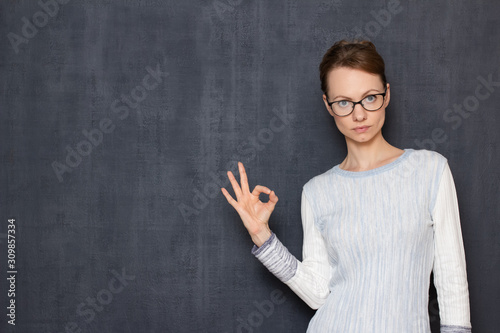 Portrait of serious woman with glasses, showing okay gesture or zero