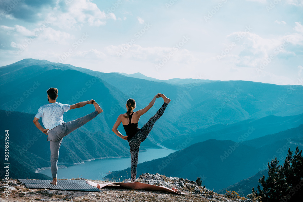 Young couple is practicing yoga at mountain lake Young couple is practicing yoga at mountain lake