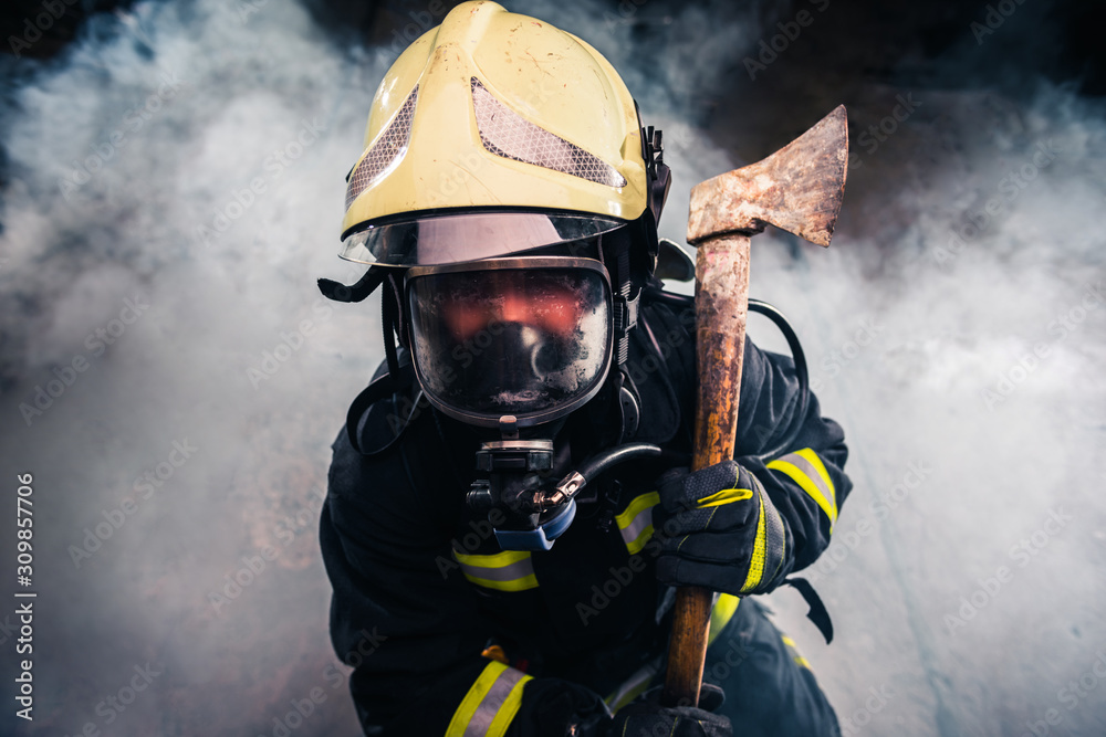 Obraz premium Portrait of a female firefighter while holding an axe and wearing an oxygen mask indoors surrounded by smoke.
