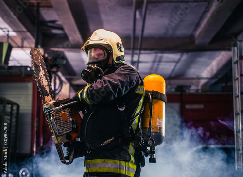 Portrait of young fireman standing and holding a chainsaw in the middle of the chainsaw's smoke .