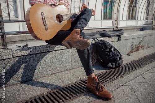 Young guitarist sitting and resting with guitar outdoors