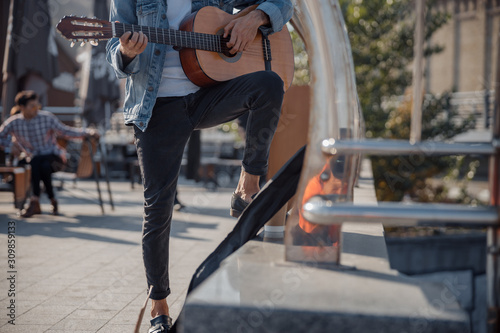 Young guy holding guitar and playing on the street