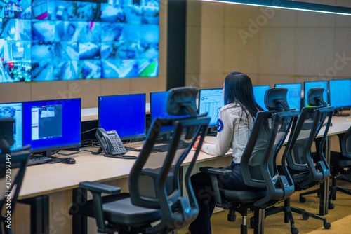 Female security guard sitting back and monitoring modern CCTV cameras in a surveillance room.