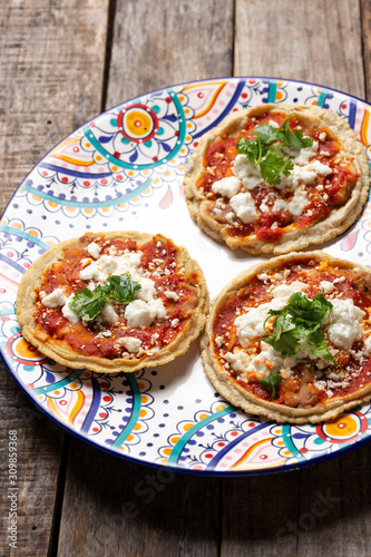 Mexican sopes with red sauce and fresh cheese on wooden background