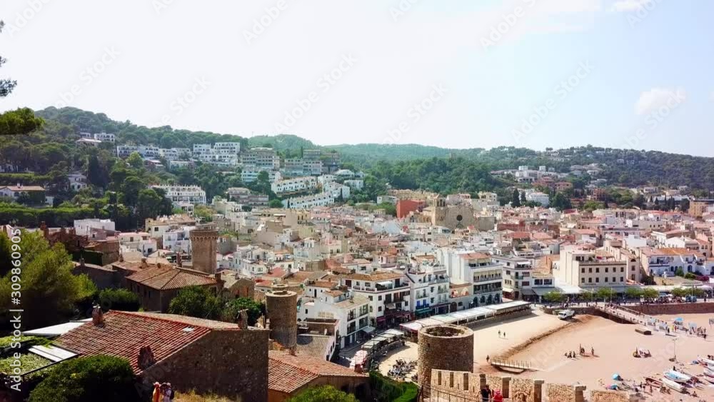 Aerial, rising, drone shot, over the castle, towards the Tossa de Mar village and the Riera de Tossa beach, on a sunny, summer day, in Catalonia, Spain Aerial, rising, drone shot, over the castle, towards the Tossa de Mar village and the Riera de Tossa beach, on a sunny, summer day, in Catalonia, Spain