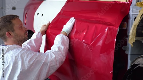 worker man is covering doors of automobile by tape, during repair works