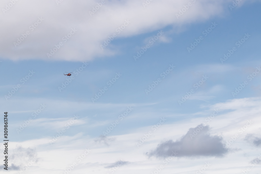 Fototapeta premium A helicopter flies through the blue sky among white clouds