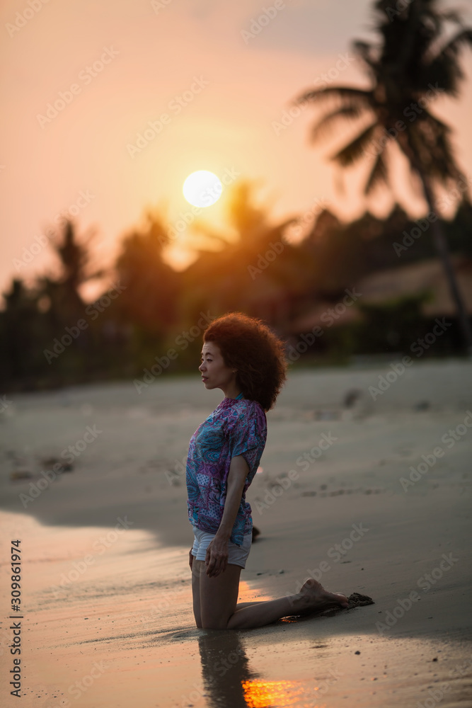 Young asian woman kneel on the surf line on the sea beach during amazing sunset.
