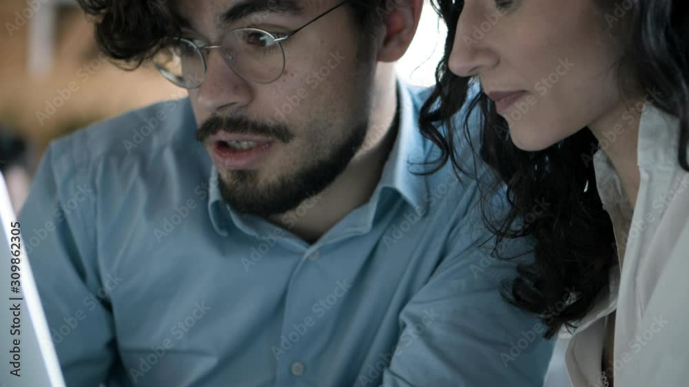Closeup shot of focused young woman talking with confident colleague. Concentrated male and female coworkers sitting at table with laptop in open space office. Technology concept Closeup shot of focused young woman talking with confident colleague. Concentrated male and female coworkers sitting at table with laptop in open space office. Technology concept