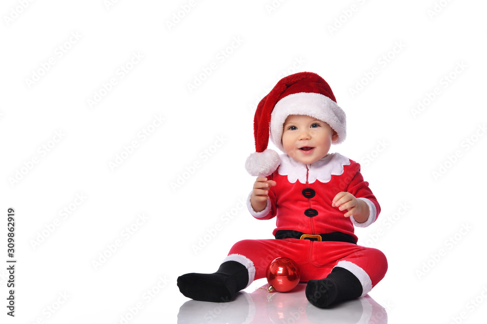 Little child boy toddler in santa claus christmas costume and hat happy smiling with red gift ball fir decoration ready to celebrate Little child boy toddler in santa claus christmas costume and hat happy smiling with red gift ball fir decoration ready to celebrate