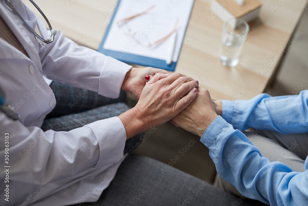 High angle close up of unrecognizable female doctor holding hands of mature woman while comforting her during consultation in medical clinic, copy space