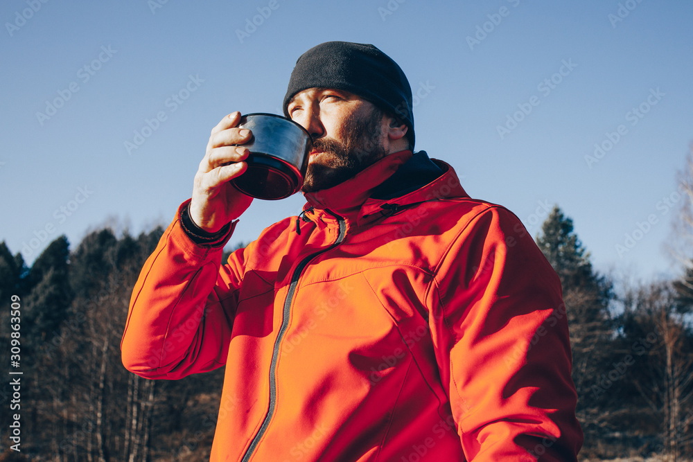 A lone tramp traveler stands on ice and drinks tea from a thermos. A lone tramp traveler stands on ice and drinks tea from a thermos.