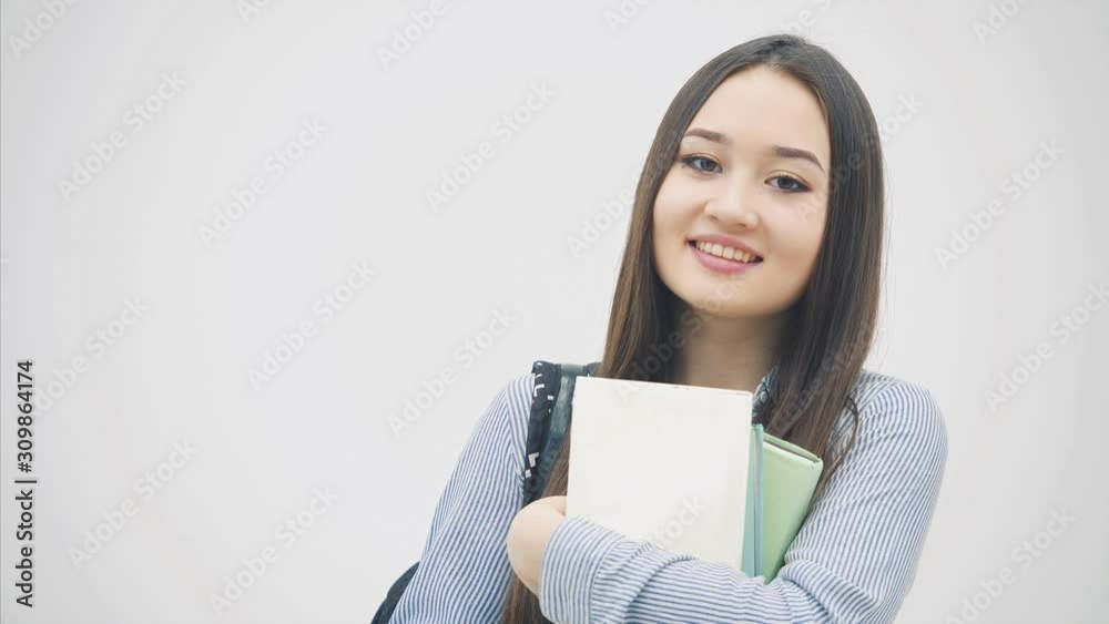 An asian schoolgirl appearing on a white background with a backpack slung over her shoulder, holding a stack of books near chest, posing, smiling. An asian schoolgirl appearing on a white background with a backpack slung over her shoulder, holding a stack of books near chest, posing, smiling.