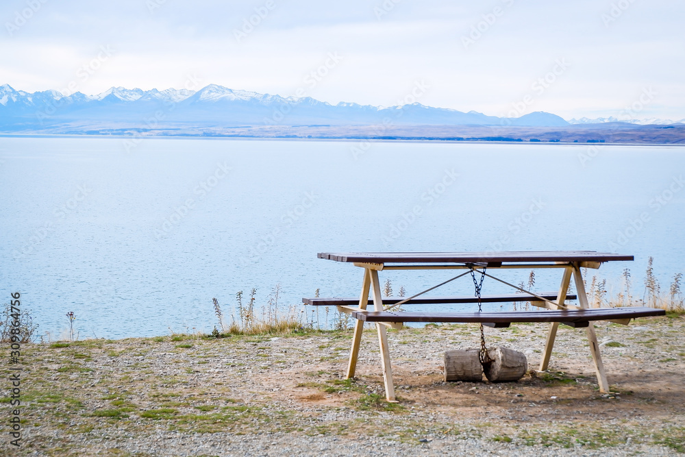 Picnic tables near mountain lake at the lake side in fall season Bench under a tree on a lake shore. Mountains at background. Take a rest near blue green lake. Beautiful mystical lake. Picnic tables near mountain lake at the lake side in fall season Bench under a tree on a lake shore. Mountains at background. Take a rest near blue green lake. Beautiful mystical lake.