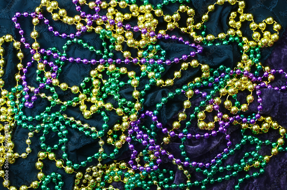 Mardi Gras background image of green, gold and purple beads on green and purple fabric.