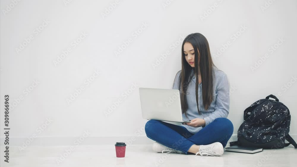 Lovely young asian lady sitting on the floor in lotos position, searching in the internet, waving hello. School supplies around her. Lovely young asian lady sitting on the floor in lotos position, searching in the internet, waving hello. School supplies around her.