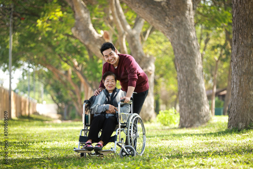 Asian senior woman sitting on the wheelchair with her son happy smile face on the green park