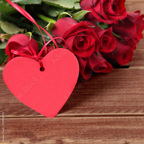 Valentine background of gift tag and red roses on wood. Space for copy.
