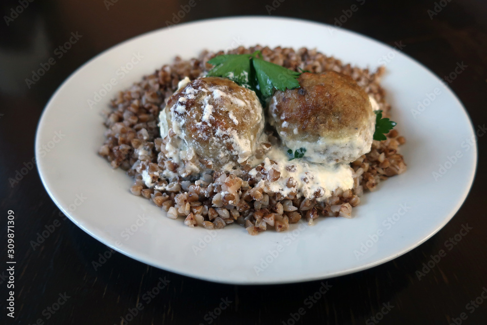 two cutlets with buckwheat porridge, poured with sauce on a white plate two cutlets with buckwheat porridge, poured with sauce on a white plate