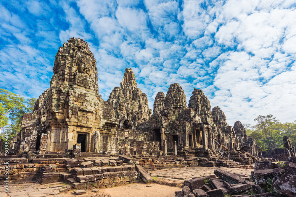 Bayon temple with cloud, blue sky and tourist in Angkor wat Angkor thom area, Siem reap of Cambodia. Prasat Bayon most smiling stone faces on the many towers. Bayon temple with cloud, blue sky and tourist in Angkor wat Angkor thom area, Siem reap of Cambodia. Prasat Bayon most smiling stone faces on the many towers.