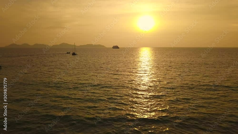 Aerial push-in shot of sun setting over sea in Thailand, boats and distant island visible