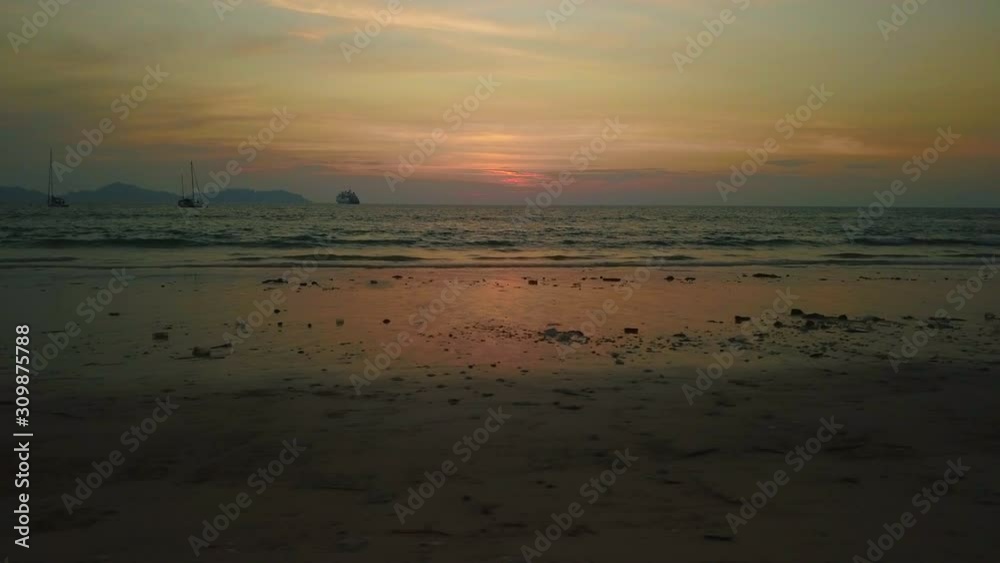 Aerial slide along beach in Thailand as sun sets over ocean by distant horizon Aerial slide along beach in Thailand as sun sets over ocean by distant horizon