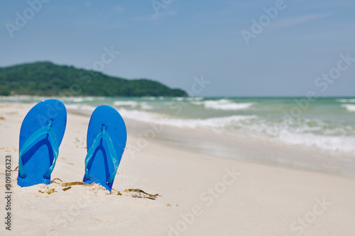 Bright blue flip-flops in sand on the beach, sea waves in background