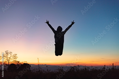 Silhouette of happy people jumping playing on mountain at sunset