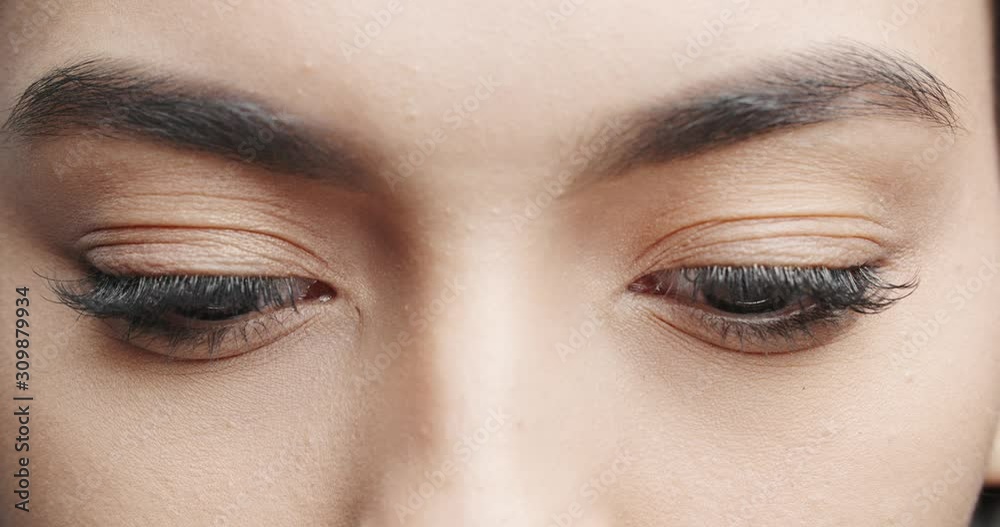 Close up shot of female eyes with makeup on eyelashes and dark brown irises looking around, isolated on black background 4k footage