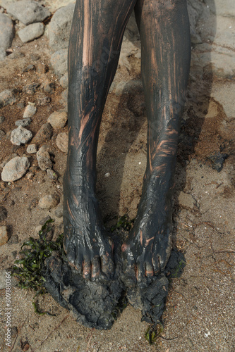 A natural resorts and spa. Woman's legs are smeared with black healing mud in the sand at the source