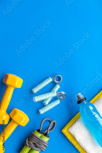 Gym equipment - dumbbells, jump rope - frame on blue background top-down copy space